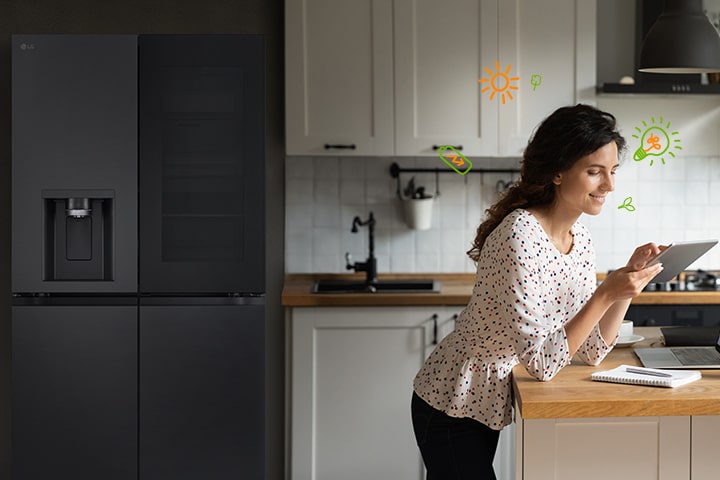 Frente al refrigerador, la mujer sonríe mientras mira la cuenta, y hay ampolletas e íconos de naturaleza alrededor de la mujer que representan la eficiencia energética.