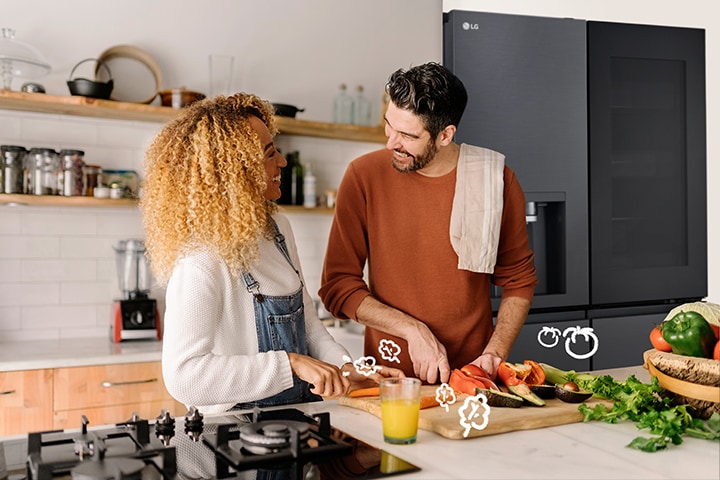 La pareja sonriente cocina frente al refrigerador.