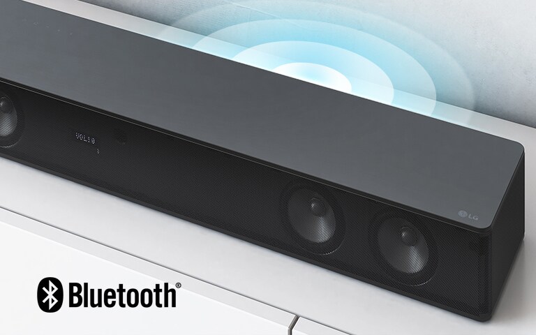 La barra de sonido LG está en un estante blanco. Un gráfico de sonido sale del altavoz. El logotipo de LG se muestra en la esquina derecha de la barra de sonido.