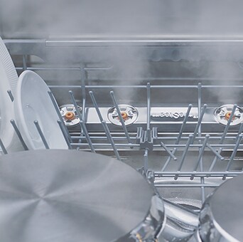 Primer plano de platos y vasos siendo lavados al vapor dentro del lavavajillas.