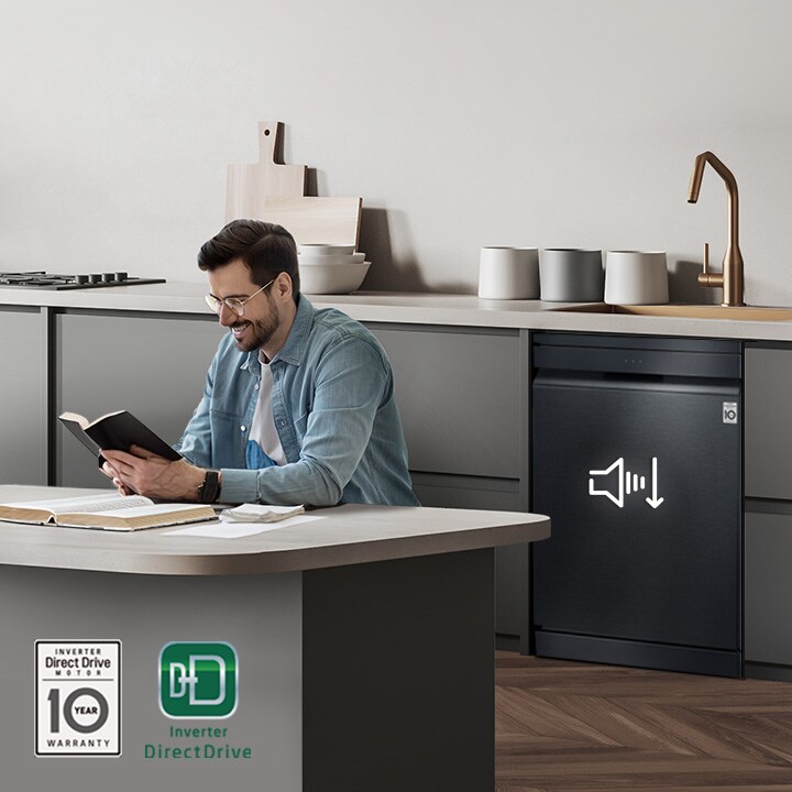 Un hombre lee un libro en la isla de la cocina mientras el lavavajillas de libre instalación LG funciona de fondo.