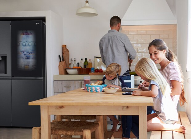 Familia sentada preparando una comida. Refrigerador InstaView instalado en un lado de la cocina genera aire frío rápidamente.