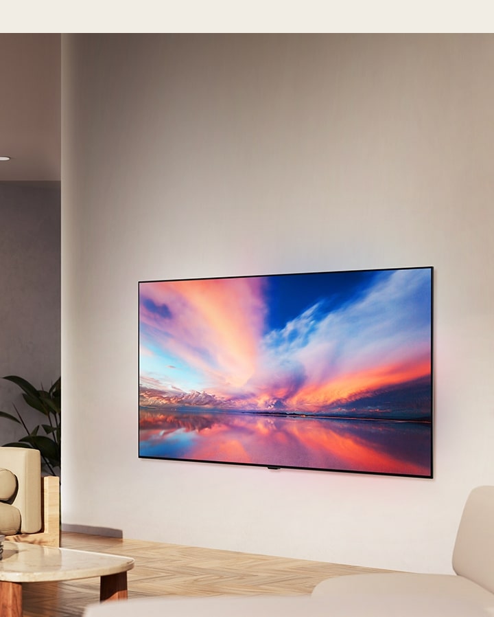 El televisor LG OLED B4 montado en la pared en un espacio neutral, mostrando una imagen colorida de un atardecer en el oceano