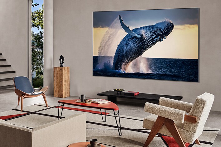 Una sala de estar con una televisión montada en la pared. En la pantalla se muestra una imagen de alta calidad de una ballena saltando fuera del agua.
