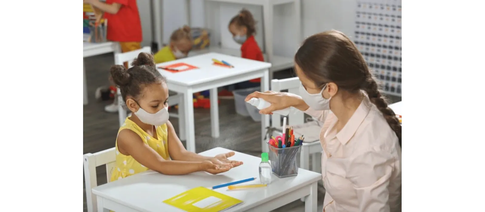 Mujer desinfectando las manos de una niña en un escritorio