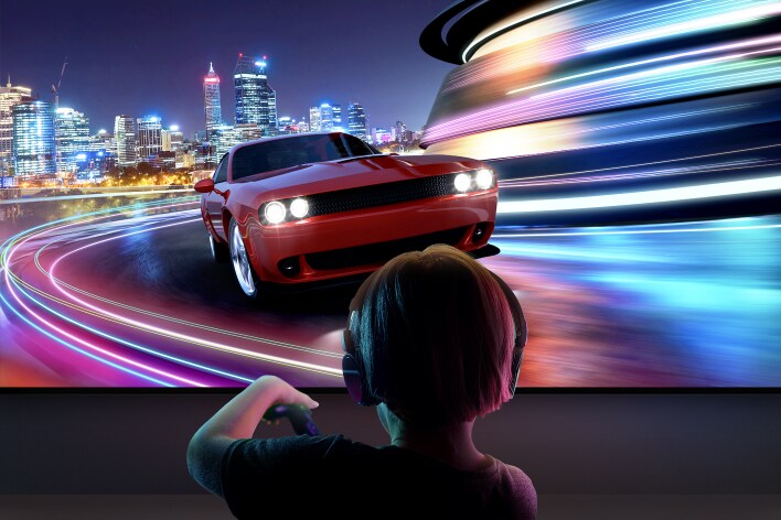 Un niño con audífonos se ve desde atrás mientras juega un videojuego de carreras de autos en un gran LG TV. 