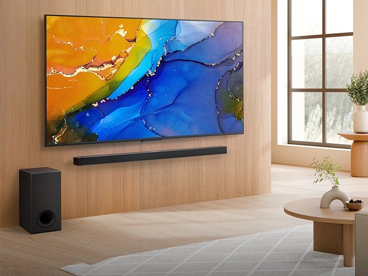 LG QNED TV namontovaný na stěně nad soundbarem LG Soundbar v moderním obývacím pokoji. LG QNED TV zobrazuje barevné pozadí.