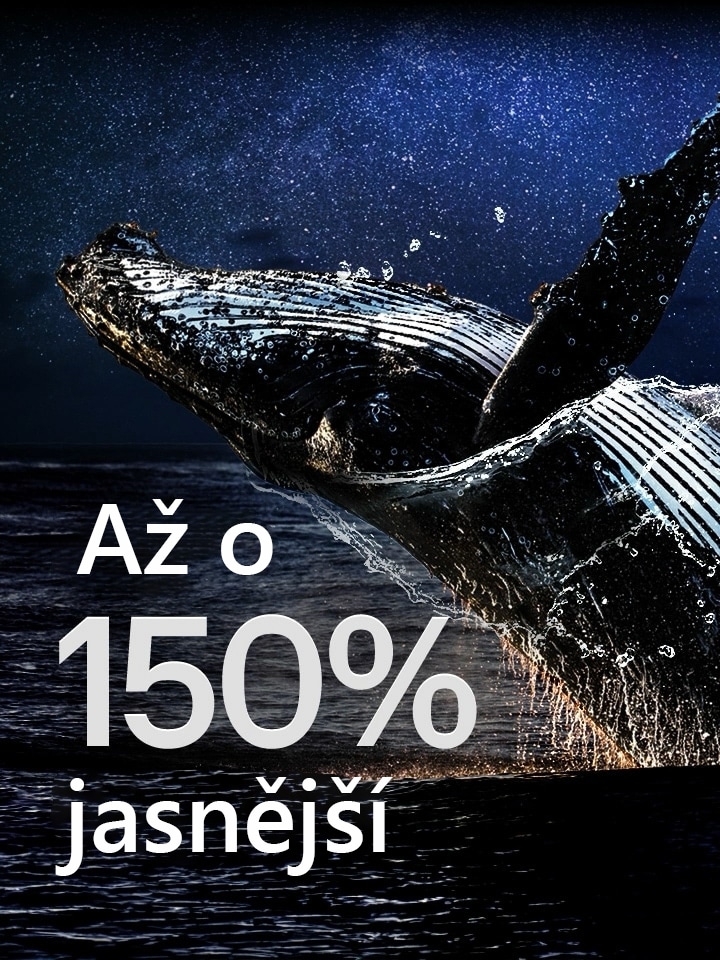 Velryba vyskakující z oceánu na černém pozadí. Nad velrybou se objeví nápis „až o 150 % jasnější“ a stane se jasnějším.