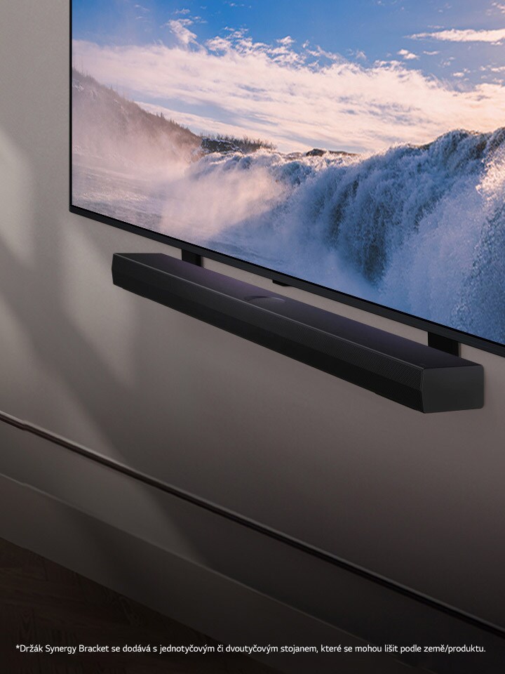 Boční pohled na televizor LG a soundbar připevněné na zdi. Na televizoru je zobrazen detail obrovského vodopádu a na stěnu, televizor a soundbar dopadá jemné sluneční světlo. Prohlášení o vyloučení odpovědnosti: „Držák Synergy Bracket se dodává s jednotyčovým či dvoutyčovým stojanem, které se mohou lišit podle země/produktu.“