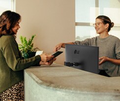 Příjemná recepční ukazuje ženě, kde se má podepsat na digitálním tabletu.	