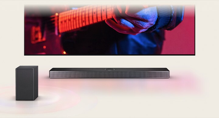 An LG TV displaying a man playing guitar and an LG Soundbar directly underneath, with another speaker in front.