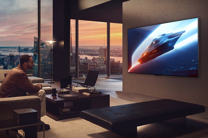 Stilvolles Wohnzimmer in einer Penthouse-Wohnung. Wunderschöne Stadtansicht durch das Fenster. Ein Mann sitzt auf der Couch und sieht auf den an der Wand befestigten Fernseher. 