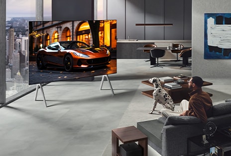 Wohnzimmer mit einem LG True Wireless TV und einer LG Soundbar, die an der Wand befestigt ist. Die Zero Connect Box ist unter einem Beistelltisch neben der Couch kaum zu sehen – sie lässt sich praktisch überall aufstellen. Das gesamte Layout des Wohnzimmers wirkt ordentlich und aufgeräumt. 