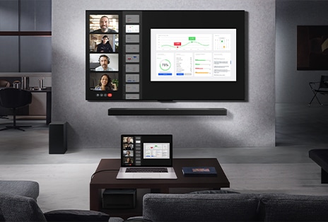 Wohnzimmer mit Blick von der Couch auf einen an der Wand montierten LG True Wireless TV und eine LG Soundbar. Auf dem Couchtisch steht ein Laptop, der mit der Zero Connect Box verbunden ist. Diese befindet sich kaum sichtbar unter dem Tisch. Der Laptop-Bildschirm, auf dem ein Live-Videoanruf läuft, wird kabellos auf den Fernsehbildschirm gespiegelt. Der gesamte Raum wirkt aufgeräumt und ist frei von Kabelsalat.