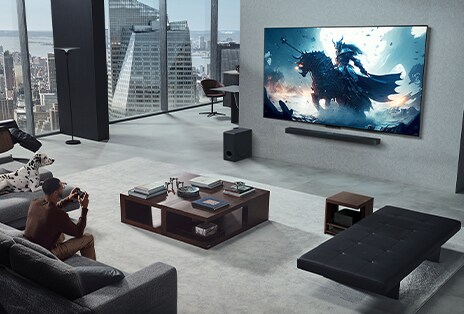 Wohnzimmer mit einer Person, die ein Video-Game auf einem an der Wand montierten LG True Wireless TV mit LG Soundbar spielt. Sie hält einen Controller in der Hand, aber die Spielkonsole ist nicht sofort zu sehen. Es sind auch keine Kabel zu sehen. Die Zero Connect Box steht versteckt unter einem Beistelltisch.