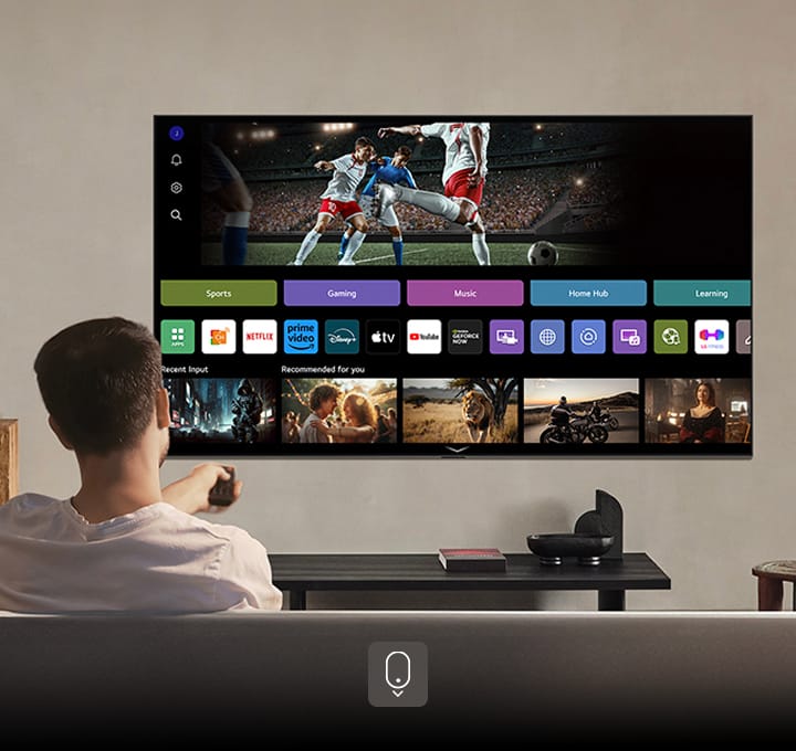 Person auf dem Sofa, die eine Fernbedienung ausrichtet. LG AI TV an der Wand mit LG webOS auf dem Bildschirm.