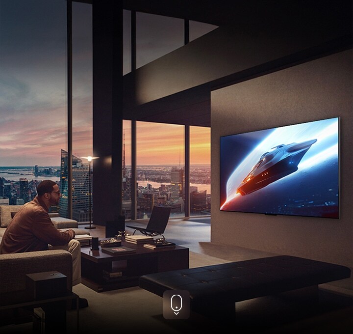 Stilvolles Wohnzimmer in einer Penthouse-Wohnung. Wunderschöne Stadtansicht durch das Fenster. Ein Mann sitzt auf der Couch und sieht auf den an der Wand befestigten Fernseher.