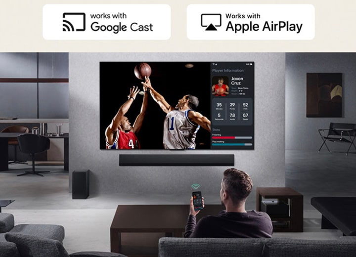 Person im Wohnzimmer, die ein Telefon in der Hand hält. Auf dem Telefon zeigt ein Übertragungssymbol an, dass der Bildschirm des Telefons auf dem Fernseher gespiegelt wird. Im Fernsehen läuft ein Basketballspiel, daneben zeigt ein Spiegelbildschirm Spielerstatistiken an.