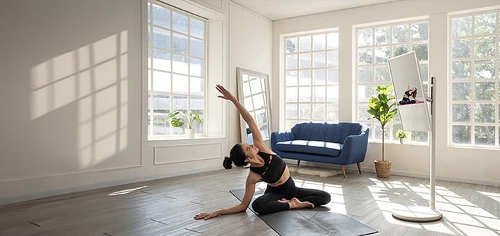Frau in ihrem geräumigen Zuhause macht Yoga. Neben ihr steht der LG StanbyME TV auf einem Standfuß. Das Gerät befindet sich in vertikaler Ausrichtung und gibt das Yoga-Unterweisungsvideo wieder, dem die Frau folgt.
