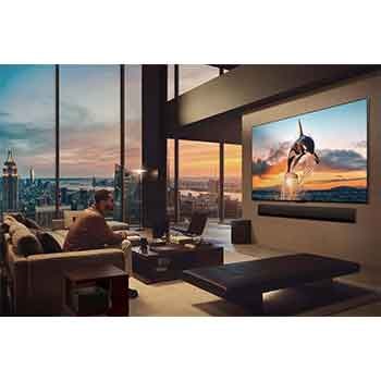 Geräumiges Wohnzimmer mit Blick auf eine Stadtlandschaft. Der LG OLED TV ist mit einer LG Soundbar an der Wand befestigt. Das flächenbündige Design des Fernsehers ermöglicht eine bündige Montage an der Wand und fügt sich gut in den Raum ein. Die Zero Connect Box ist zu sehen, aber unauffällig aufgestellt. 