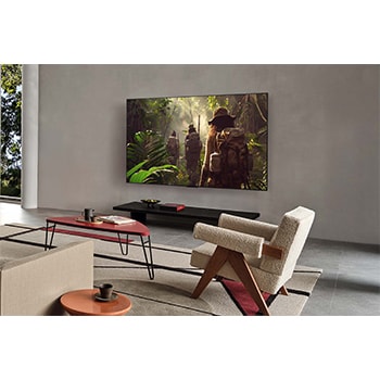 Weite Ansicht eines Wohnzimmers in einem hochwertigen Haus. Ein Mann sieht sich einen Film auf seinem an der Wand montierten LG OLED-Fernseher an. Das Design des Fernsehers fügt sich elegant in die Wand und die Inneneinrichtung ein.