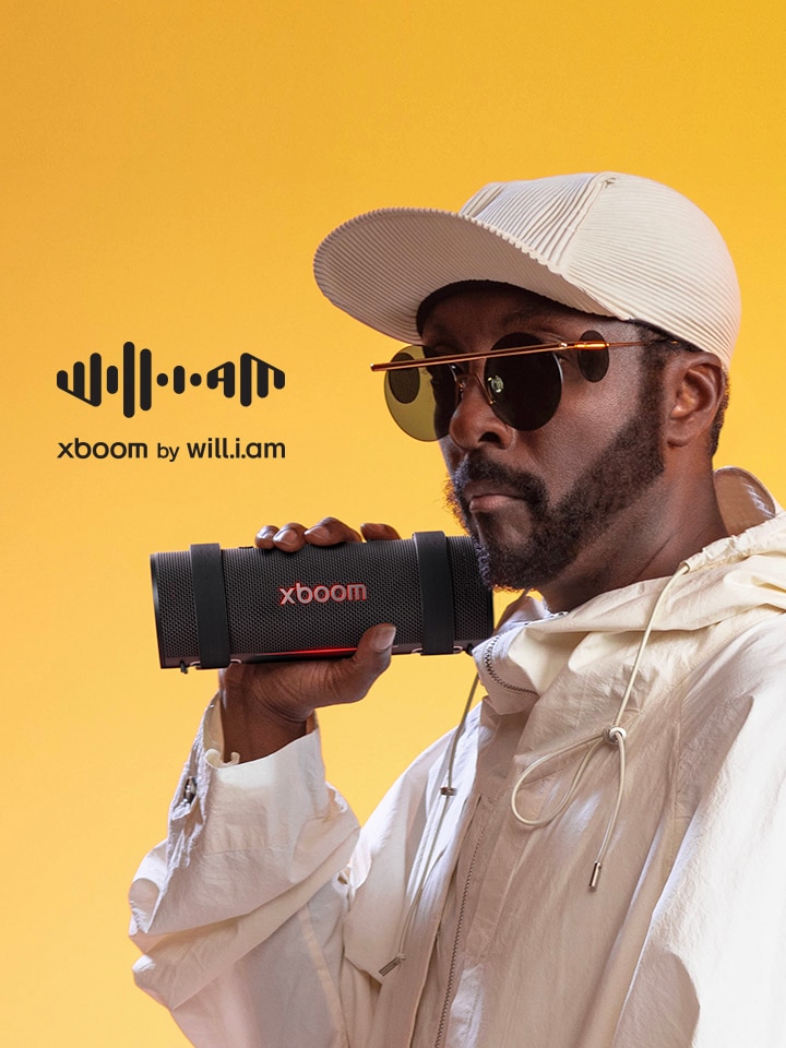 will.i.am in weißem Outfit hält xboom Grab.	