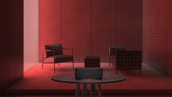 In einem Raum mit roter Beleuchtung stehen ein schwarzes Sofa, ein schwarzer Hocker und ein schwarzer Sessel. Im Vordergrund steht der xboom Bounce auf einem schwarzen runden Tisch.