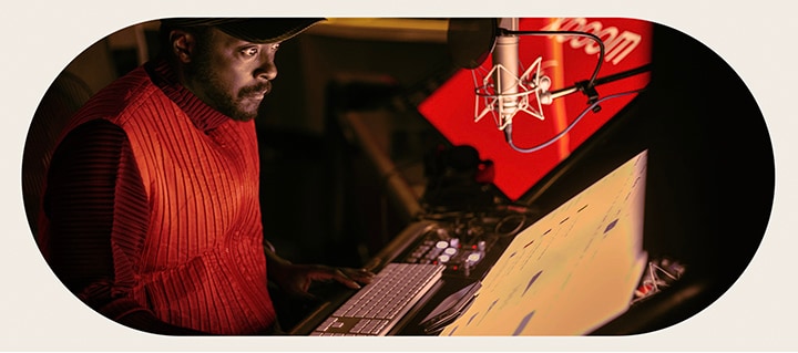 will.i.am arbeitet im Studio und schaut auf einen Bildschirm, der unter einem Mikrofon angebracht ist. 