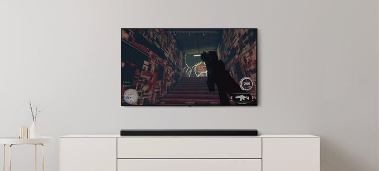 In einem Wohnzimmer befinden sich ein TV und eine Soundbar. Auf dem TV-Bildschirm läuft ein FPS-Spiel und der TV-Kanal ist auf Fußballspiel eingestellt (Video abspielen).