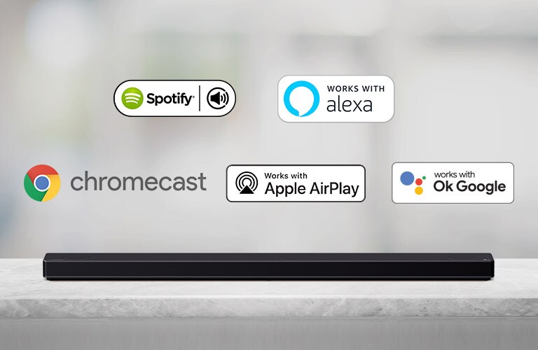 Auf einem grauen Regal steht eine Soundbar, auf der von links nach rechts die Logos von AI-Plattformen in der folgenden Reihenfolge zu sehen sind: Spotify, Alexa, Chromecast, Apple Airplay und OK Google.