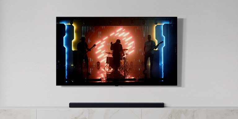 In einem hellen Wohnzimmer stehen ein TV und eine Soundbar. Auf dem TV-Bildschirm ist eine Musikband zu sehen (Video abspielen).