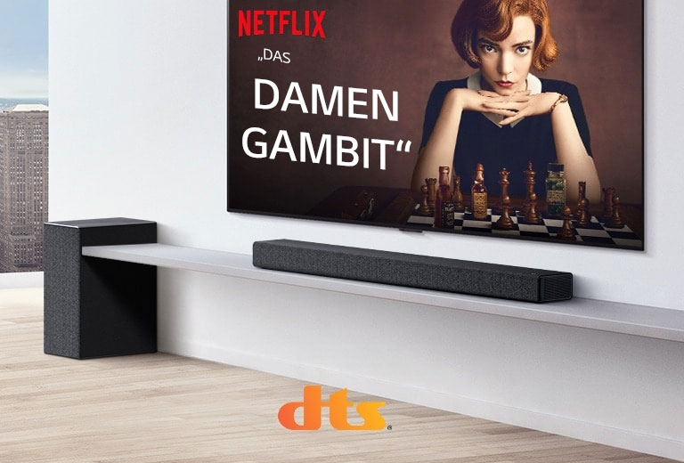 An der Wand befestigter TV. Ein Poster einer TV-Sendung ist auf dem Bildschirm zu sehen. Die LG Soundbar steht direkt unter dem TV auf einem weißen Regal mit einem Subwoofer rechts daneben. Die Logos von Dolby Atmos und DTS:X werden am mittleren unteren Bildrand gezeigt.