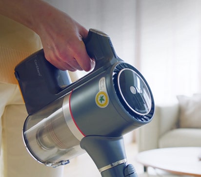 Man sieht die Hand einer Frau, die bequem den Griff des Staubsaugers ergreift, während sie das Wohnzimmer reinigt.