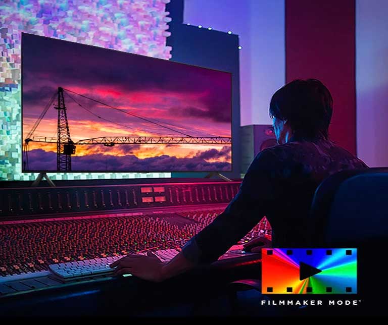 A man in a dark editing studio looking at an LG TV displaying the sunset. On the right bottom of the image is a FILMMAKER Mode logo.