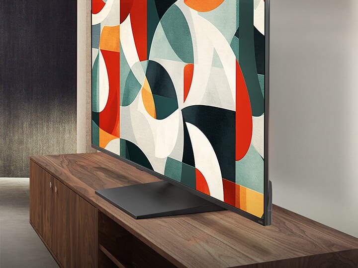 LG QNED TV steht über einer TV-Schublade in einem modernen Wohnbereich. Der LG QNED TV zeigt einen abstrakten Hintergrund in Grün, Rot und Orange.