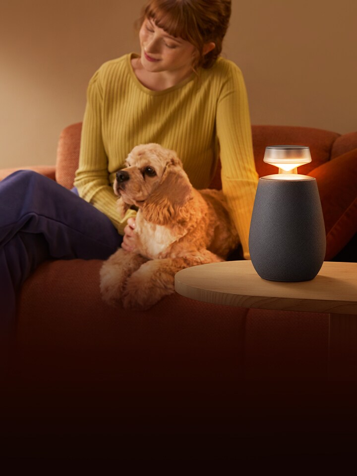 Eine Frau, die mit dem LG XBOOM XO2T und ihrem Hund auf dem Sofa entspannt.