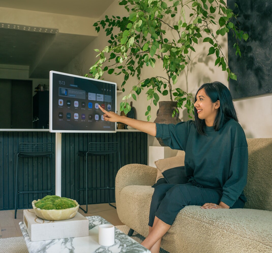 Lisa Mistry sitzt auf dem Sofa und lächelt, während sie den Bildschirm des LG StandbyME berührt.