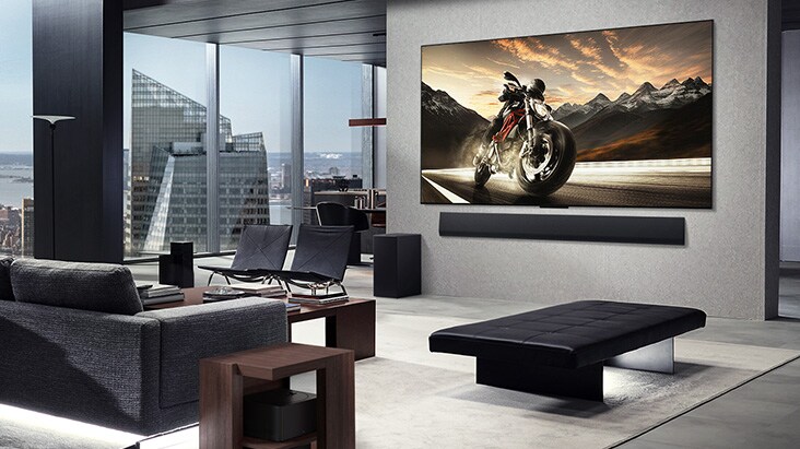 LG OLED M4 and LG Soundbar mounted on the living room wall of a high-rise apartment. The layout is clutter-free. The Zero Coonect Box can be seen, hidden underneath a side table by a couch.