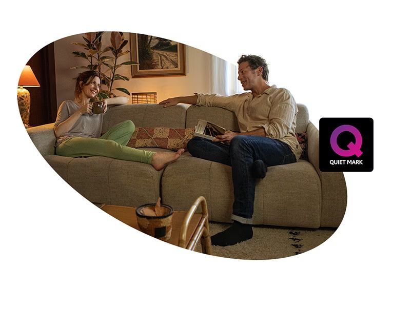 Una mujer y un hombre están sentados en un sofá hablando y sonriendo. Junto a la imagen se ve el logo de la certificación Quiet Mark.