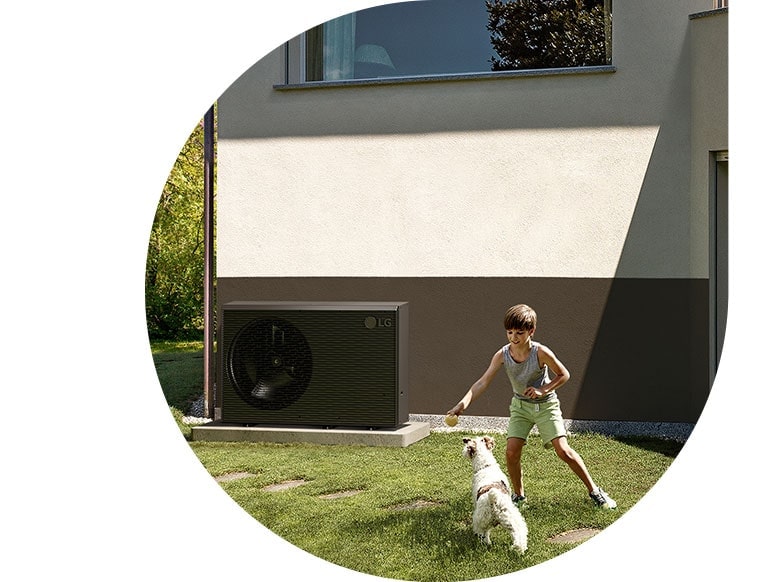 Un niño juega con el perro en el jardín de una casa en la que se ha instalado una nueva bomba negra THERMA V de LG.