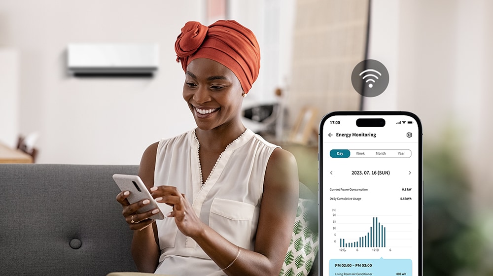 Una mujer que disfruta del viento fresco del aire acondicionado comprueba el consumo energético del aparato a través de la pantalla de la app ThinQ™.