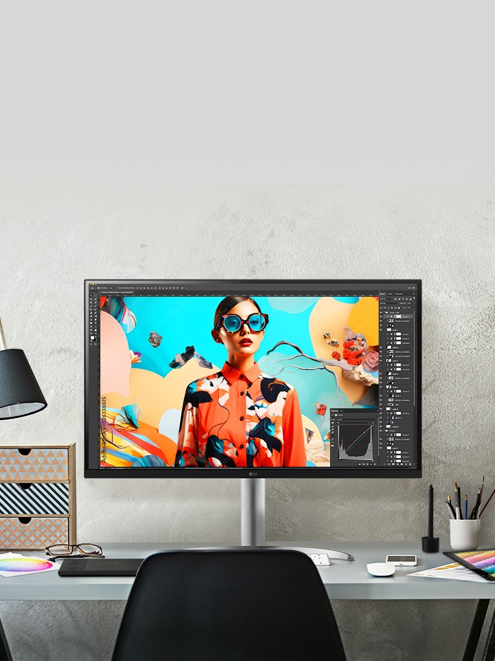 Sobre el escritorio de un estudio de diseño hay un monitor UltraFine que muestra en pantalla un trabajo por terminar en Photoshop.