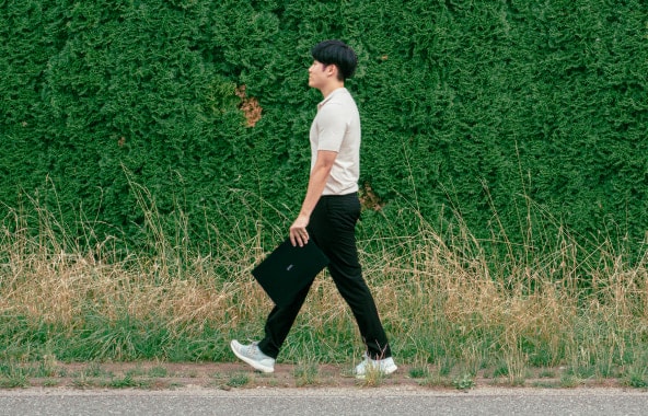 Un hombre caminando al aire libre mientras sostiene un LG gram Pro.