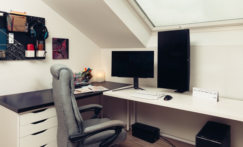 Una oficina en casa ordenada con una silla ergonómica, un escritorio con monitor vertical y suministros bien organizados.