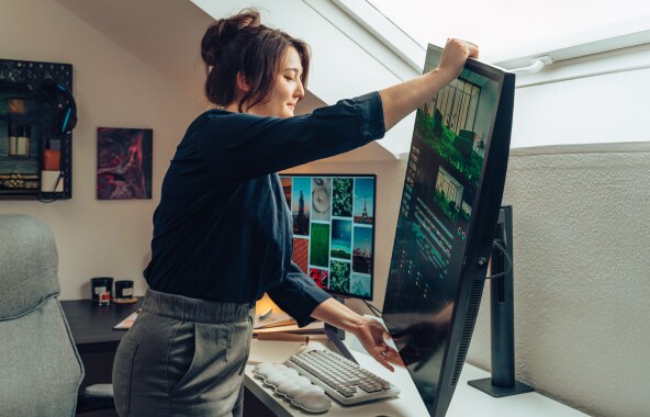 Una mujer ajusta un monitor vertical grande en una oficina en casa.