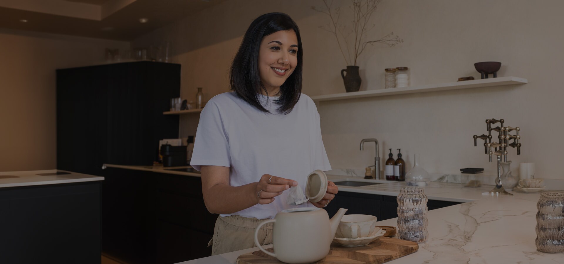 Lisa Mistry sonríe a la cámara mientras coloca una bolsita de té en la tetera en la barra del comedor.