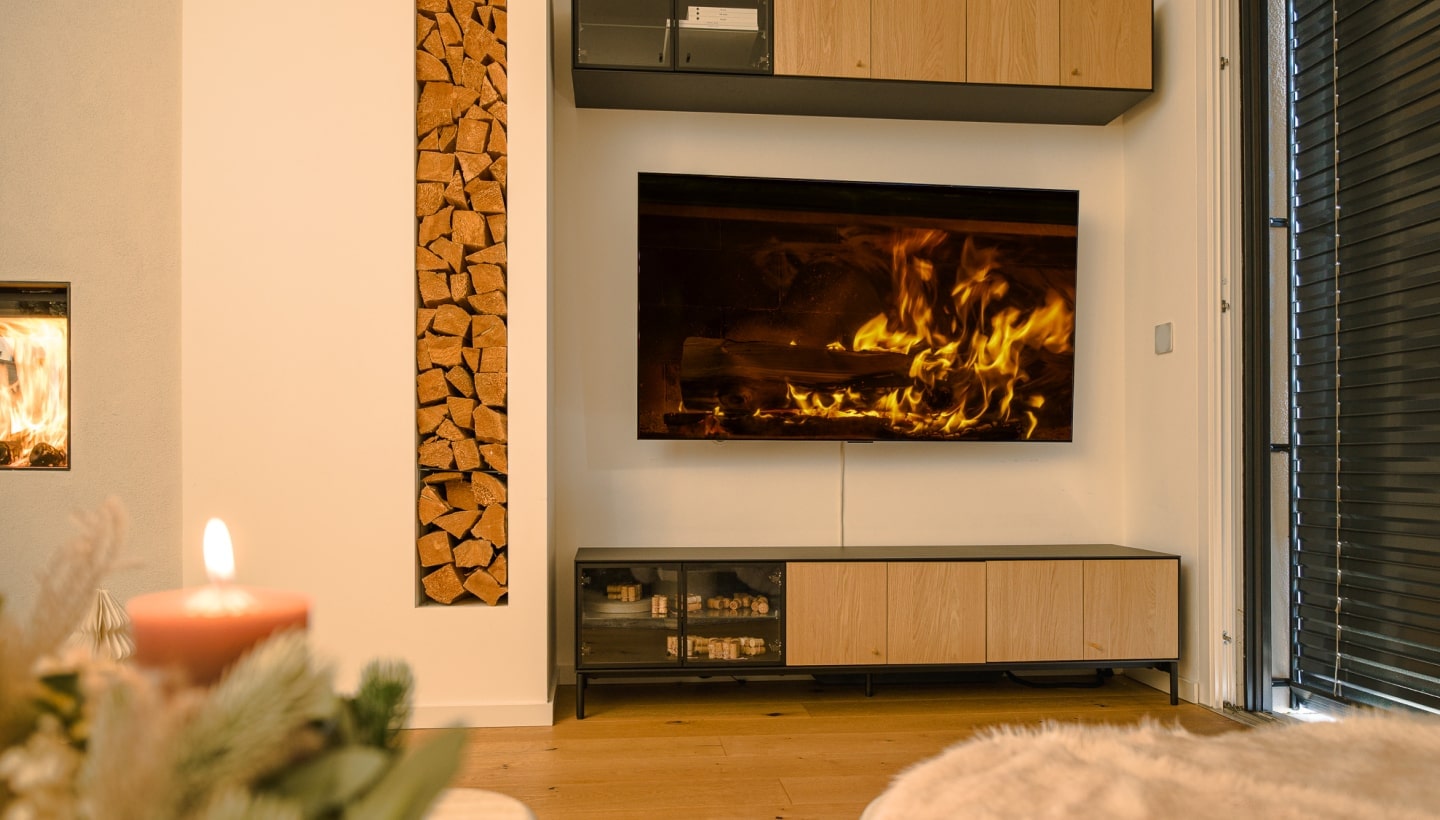 Una sala acogedora con un televisor LG OLED que muestra una chimenea virtual, muebles cómodos y velas festivas.