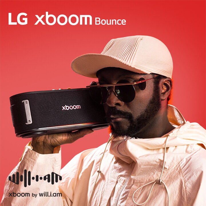 will.i.am con traje blanco y gafas de sol sostiene xboom Bounce junto a su cara.