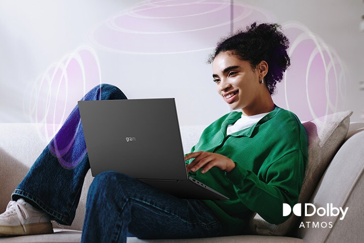 Una persona sentada en un sofá, disfrutando de audio inmersivo mientras utiliza un portátil LG gram. El texto destaca la tecnología Dolby Atmos, que enfatiza una experiencia auditiva rica, expansiva y de 360 grados. Las ondas sonoras envolventes del fondo representan visualmente el paisaje sonoro inmersivo.