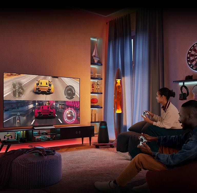 Unos hombres y mujeres están sentados en el sofá disfrutando juntos de unos juegos de carreras en el TV.